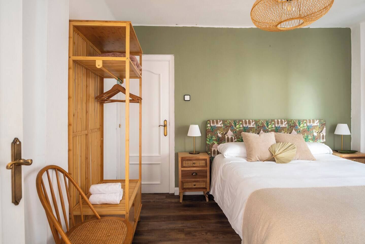 A bedroom with a bunk bed, a single bed with a patterned headboard, bedside lamps, and a wicker hanging chair.