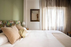 A neatly made bed with pillows and a decorative fan, a bedside lamp, a mirror on the wall, and sheer curtains. - Casa Camilo - Retro con Encanto (Santander)