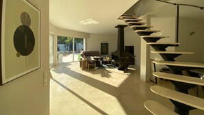 A modern living room with a curved staircase, a fireplace, and a large window overlooking a patio. - Amazing villa 10 min to Monaco (Roquebrune-Cap-Martin)