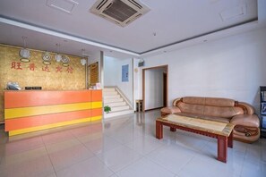 A reception area with a reception desk, a sofa, a coffee table, and a staircase in the background. - Wangpuda Hostel (Shanghai)