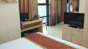 Habitació d'hotel amb un llit, un escriptori amb un ordinador, televisió i una finestra amb cortines.