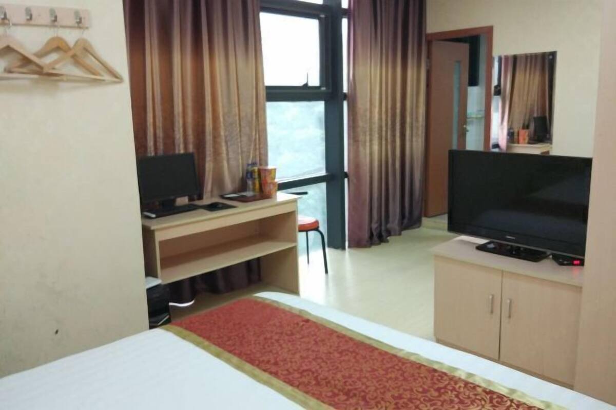 A hotel room with a bed, a desk with a computer, a television, and a window with curtains.