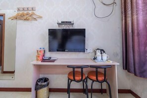 Una habitación pequeña con televisión, escritorio, dos sillas, cubo de basura y perchero.