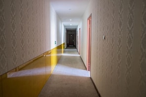A long, narrow hallway with patterned walls and a carpeted floor, leading to a door at the end. - Wangpuda Hostel (Shanghai)