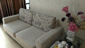 Un sofà beix amb coixins florals, un ram de flors en un vas i un petit taula amb diferents objectes.