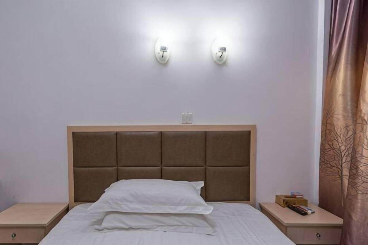 A hotel room with a bed, two bedside tables, and wall-mounted lights.