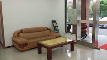 Quarto com sofá, mesa de centro, janela com vista para a rua e porta com painel de vidro.