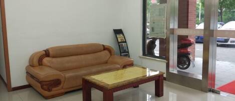A room with a sofa and a coffee table, a window with a view of the street, and a door with a glass panel.