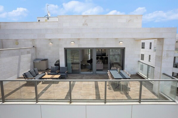 A rooftop terrace with outdoor seating, a sliding glass door entrance, and a view of the cityscape.