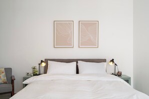 A neatly made bed with white linens, two bedside lamps, and a wall-mounted artwork above it.