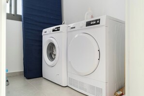 A laundry area with two white front-loading washing machines and a blue drying rack.