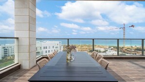 A balcony with a table set for two, overlooking a coastal view with buildings and a crane in the distance. - Mamad Achziv Seaside Stylish Stay (Nahariya)