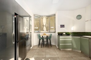 A compact kitchen with a corner dining area, a refrigerator, and a clock on the wall.