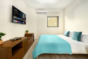 A bedroom with a bed, a desk, a TV mounted on the wall, and a window.
