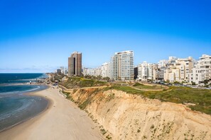 Un paysage urbain côtier avec de hauts immeubles, une plage de sable et un ciel bleu dégagé.