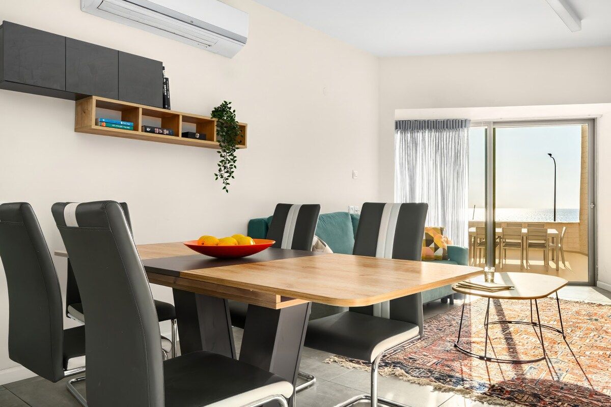 Een moderne eetruimte met een houten tafel, zwarte stoelen en een kleurrijk vloerkleed.