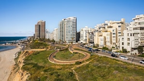 Une zone urbaine côtière caractérisée par de grands immeubles, une plage et un parc aménagé avec une route sinueuse.