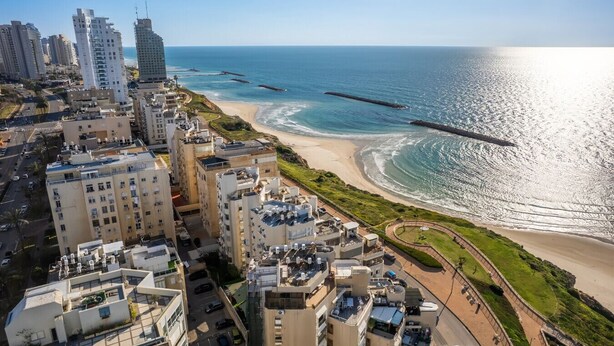 Un paysage urbain côtier avec de hauts immeubles, une plage et un ciel dégagé.