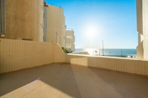 Un balcon spacieux avec vue sur la mer, un sol carrelé et un bâtiment doté d’un toit plat.