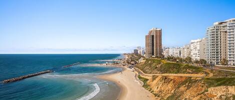 A coastal cityscape with a beach, high-rise buildings, and a clear sky.
