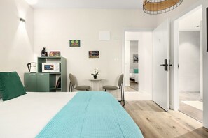 Una camera da letto con un letto, una scrivania, una sedia, un piccolo tavolo con una pianta e una porta che dà su un'altra stanza.