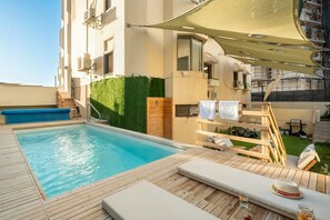 Una piscina sul tetto con un solarium in legno, poltroncine relax e una zona salotto coperta.
