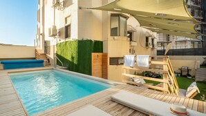 Une piscine sur le toit, dotée d’une terrasse en bois, de chaises longues et d’un espace salon abrité.