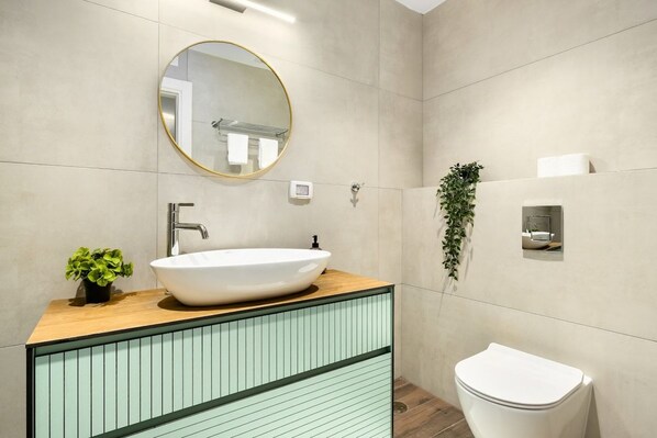A bathroom with a round mirror, a white sink, a toilet, and a small plant.