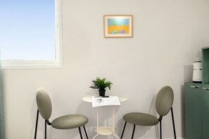 Una stanza con una finestra, un quadro incorniciato, un tavolino con una pianta e due sedie.