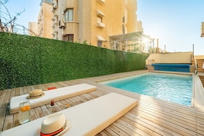 Ein Pool auf dem Dach mit Holzterrasse, Liegestühlen und einer grünen Hecke.