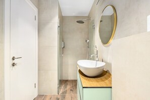 Un bagno moderno con un ampio specchio ovale, un mobile bagno in legno e una cabina doccia in vetro.