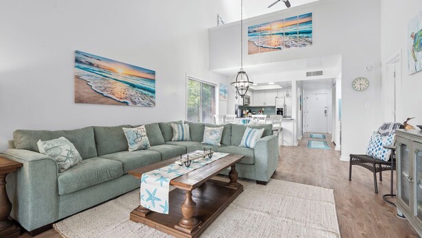 A spacious living room with a green sectional sofa, a wooden coffee table, and a kitchen in the background. - Coastal Penthouse Paradise Indoor Heated Pool Marsh View (Myrtle Beach)