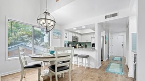 A modern kitchen with white cabinets, a central island, and a dining area with a round table and chairs. - Coastal Penthouse Paradise Indoor Heated Pool Marsh View (Myrtle Beach)