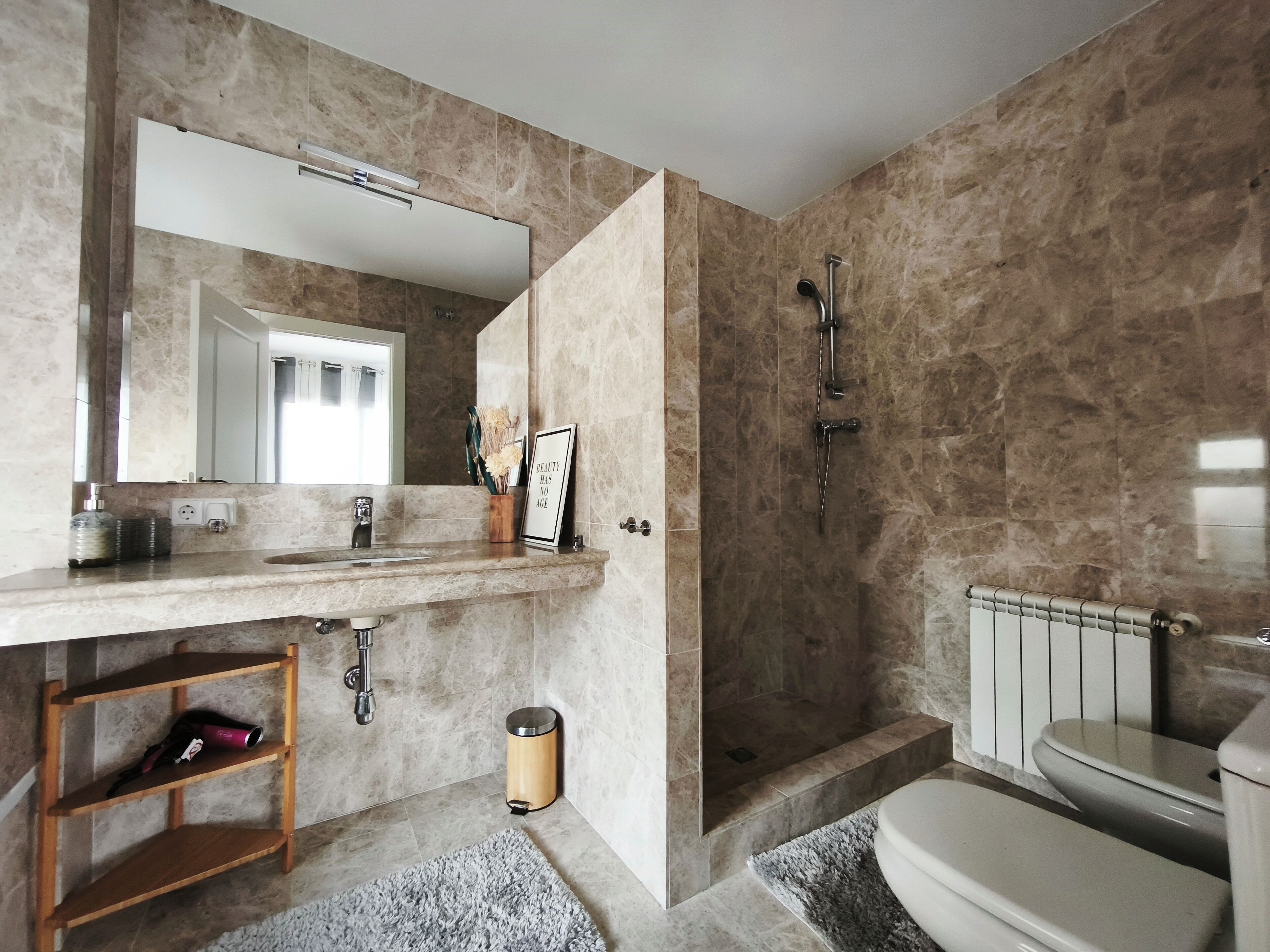 A bathroom with a marble sink, a mirror, a shower, and a toilet.