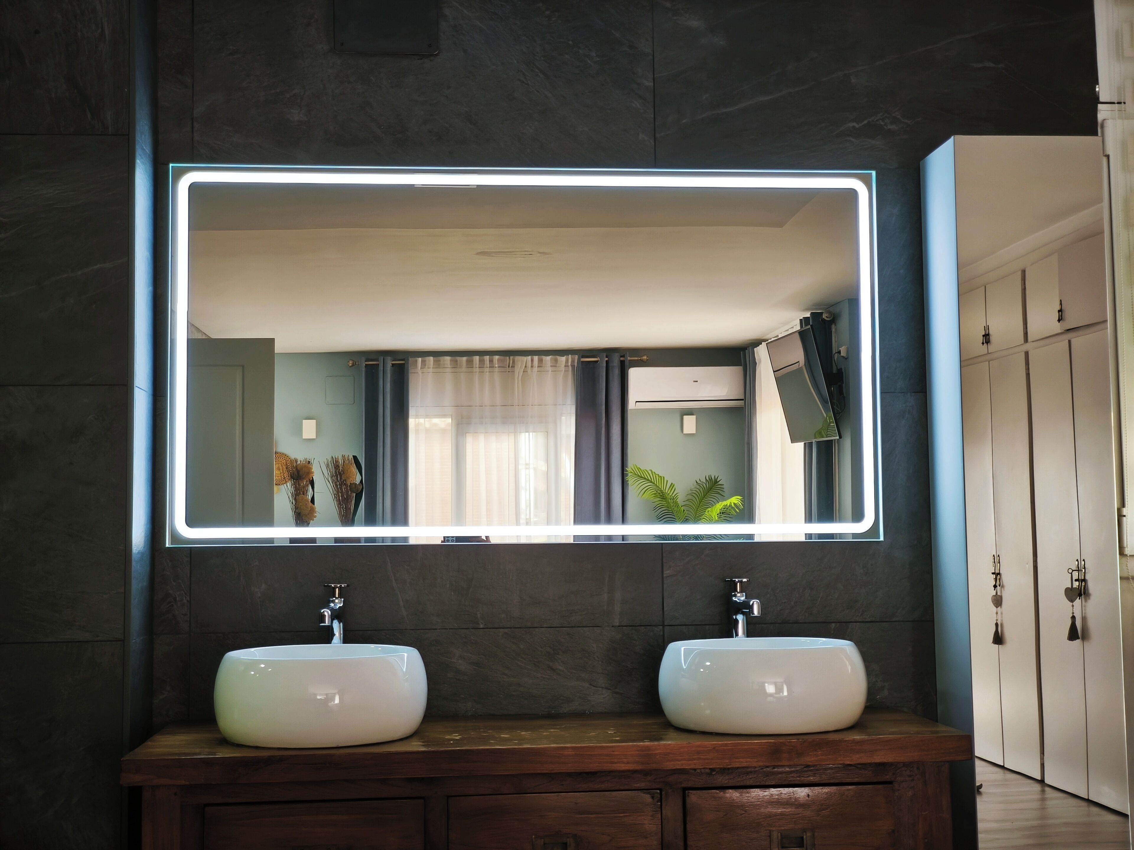 Ein Badezimmer mit zwei weißen Waschbecken, einem großen Spiegel mit LED-Beleuchtung und einer dunklen Holzkommode.