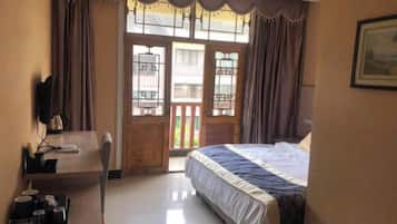Un dormitorio con cama, escritorio y silla. Hay una ventana con cortinas y una puerta que da a un espacio exterior.