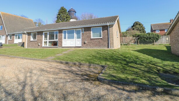 Une maison à deux étages, construite en briques, avec un toit en tuiles, un porche à l’avant et un petit jardin.