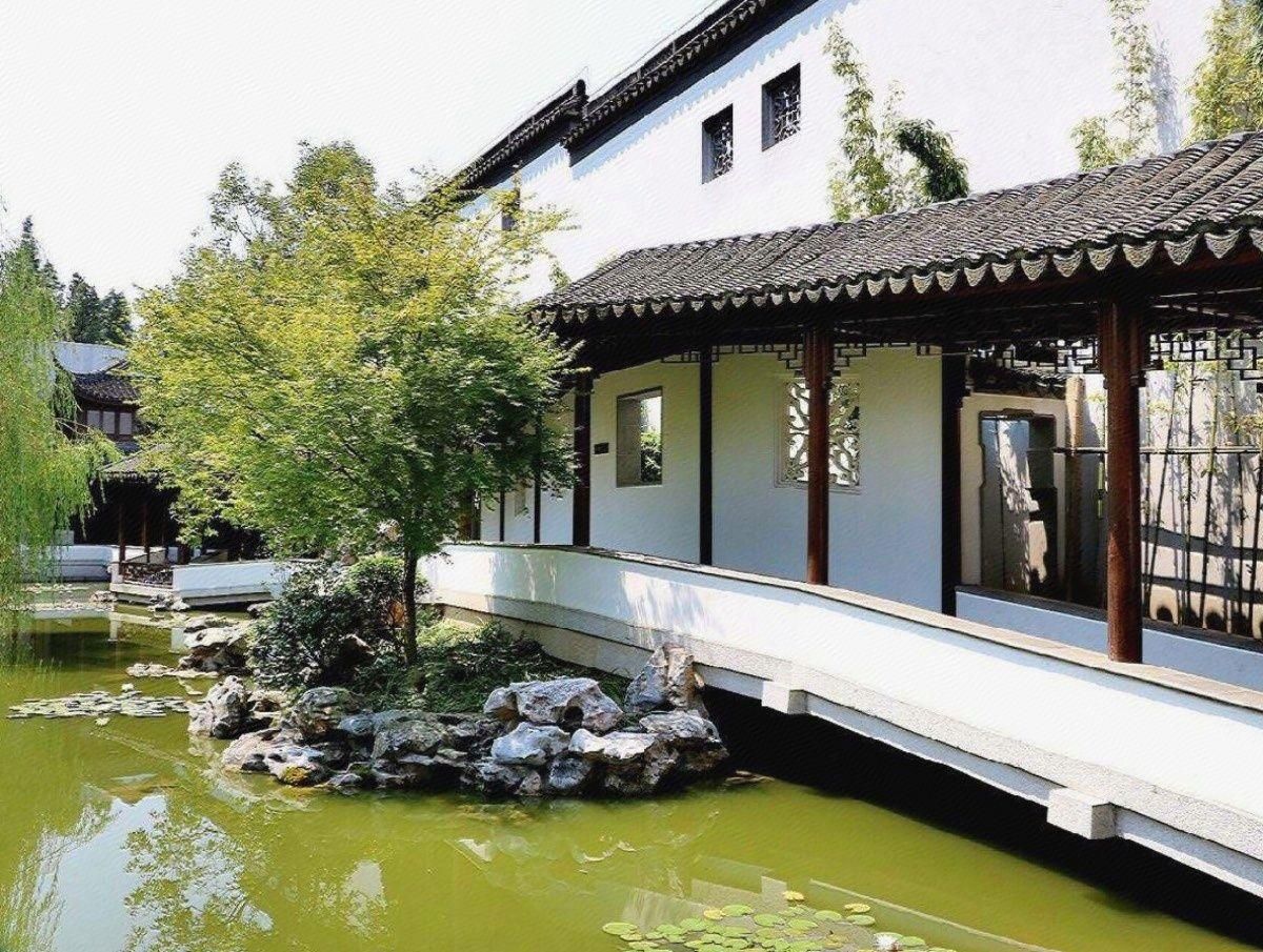 A traditional building with a tiled roof, a stone bridge, and a pond with rocks and plants.