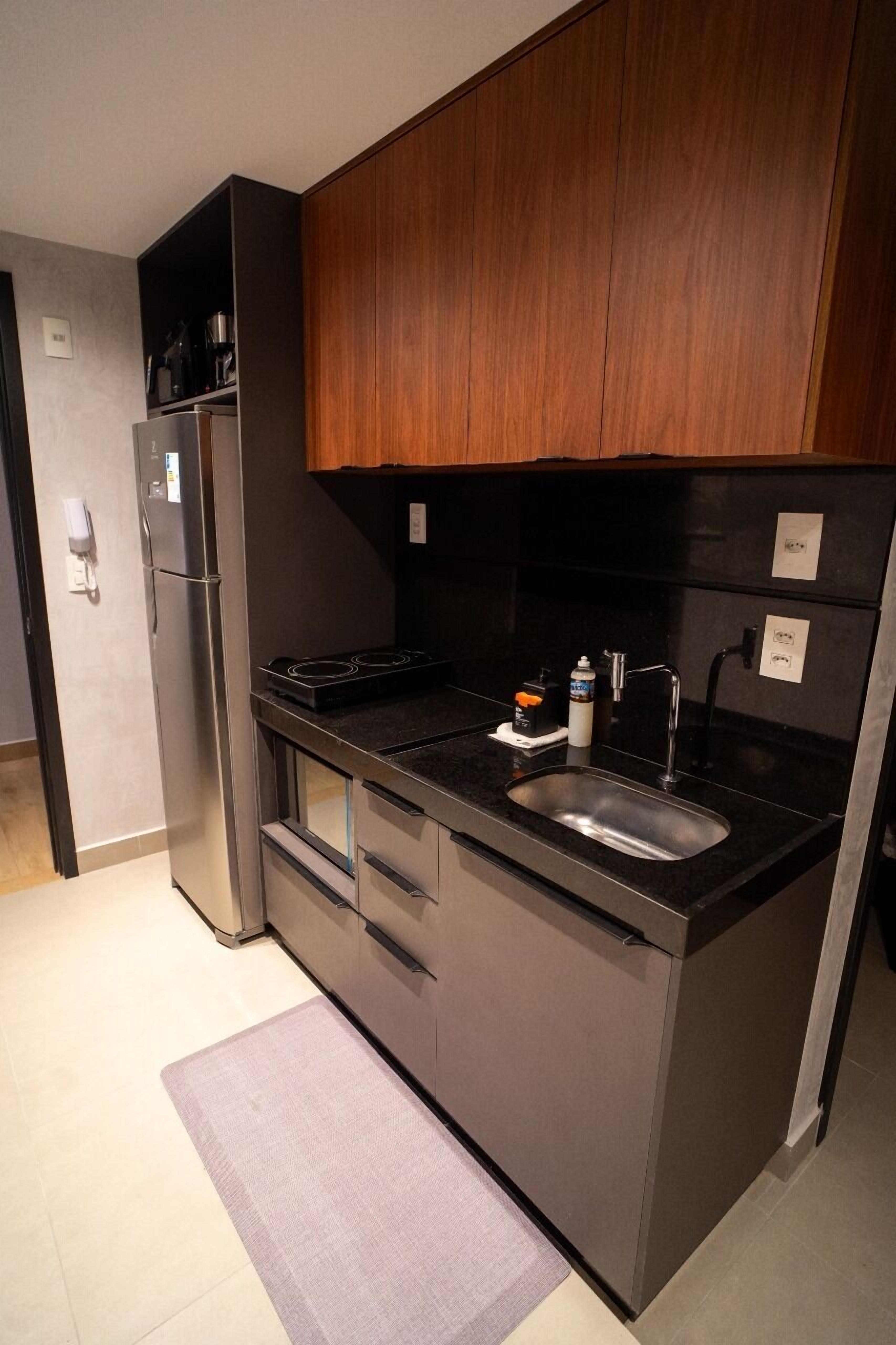A compact kitchen with a refrigerator, stove, sink, and wooden cabinets.