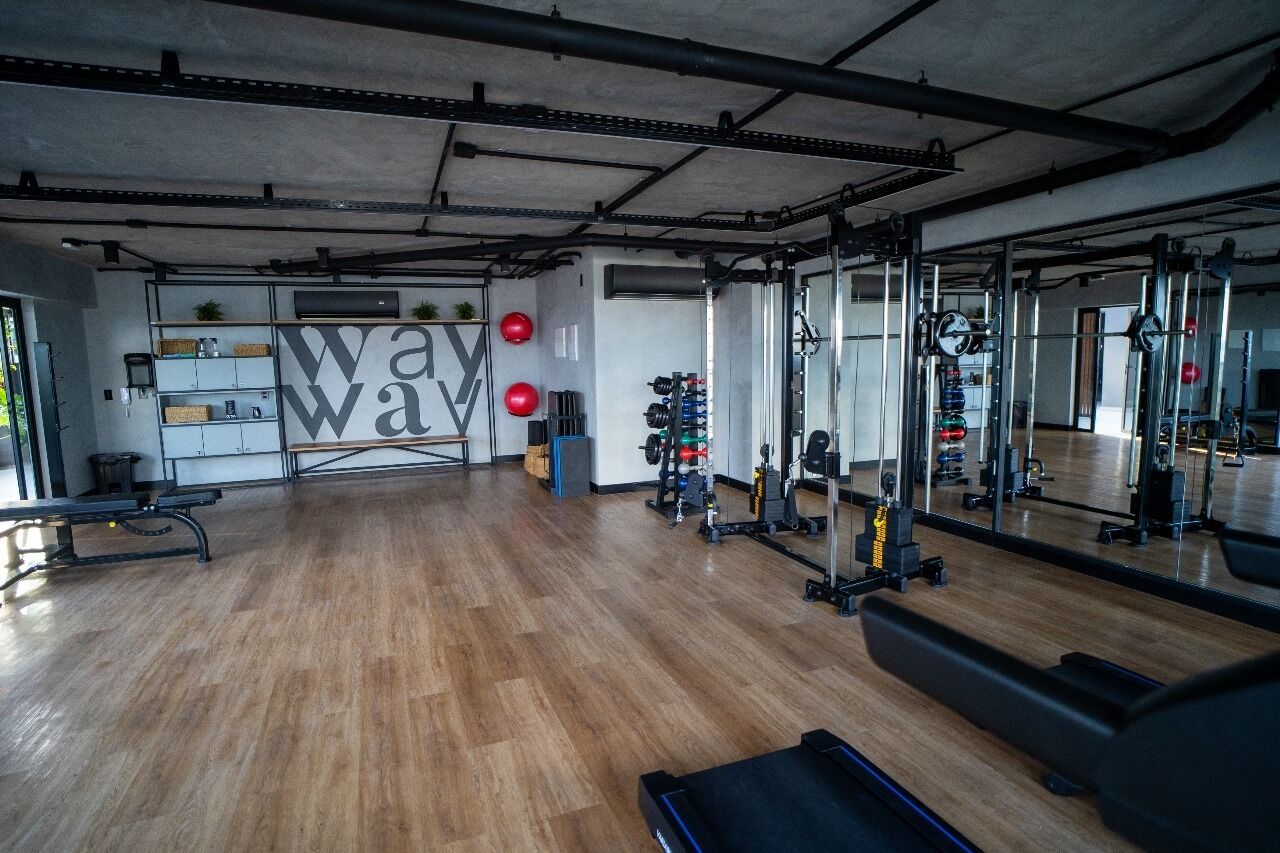 Et trægulvs fitnesscenter med træningsudstyr og et stort spejl.