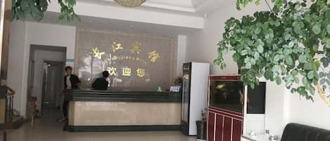 A hotel reception area with a reception desk, a chandelier, and a large plant.
