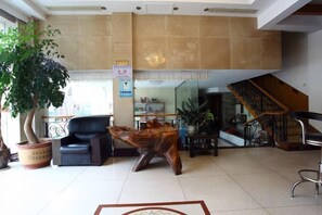 A lobby with a reception desk, a staircase, a black leather chair, a wooden sculpture, and a potted plant. - Changjiang Hotel (Ningbo)
