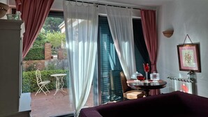 A room with a bed, a table with a glass, and a chair. There is a window with curtains, and a view of a garden outside. - Luxury villa in residence in Sicily  (Messina)