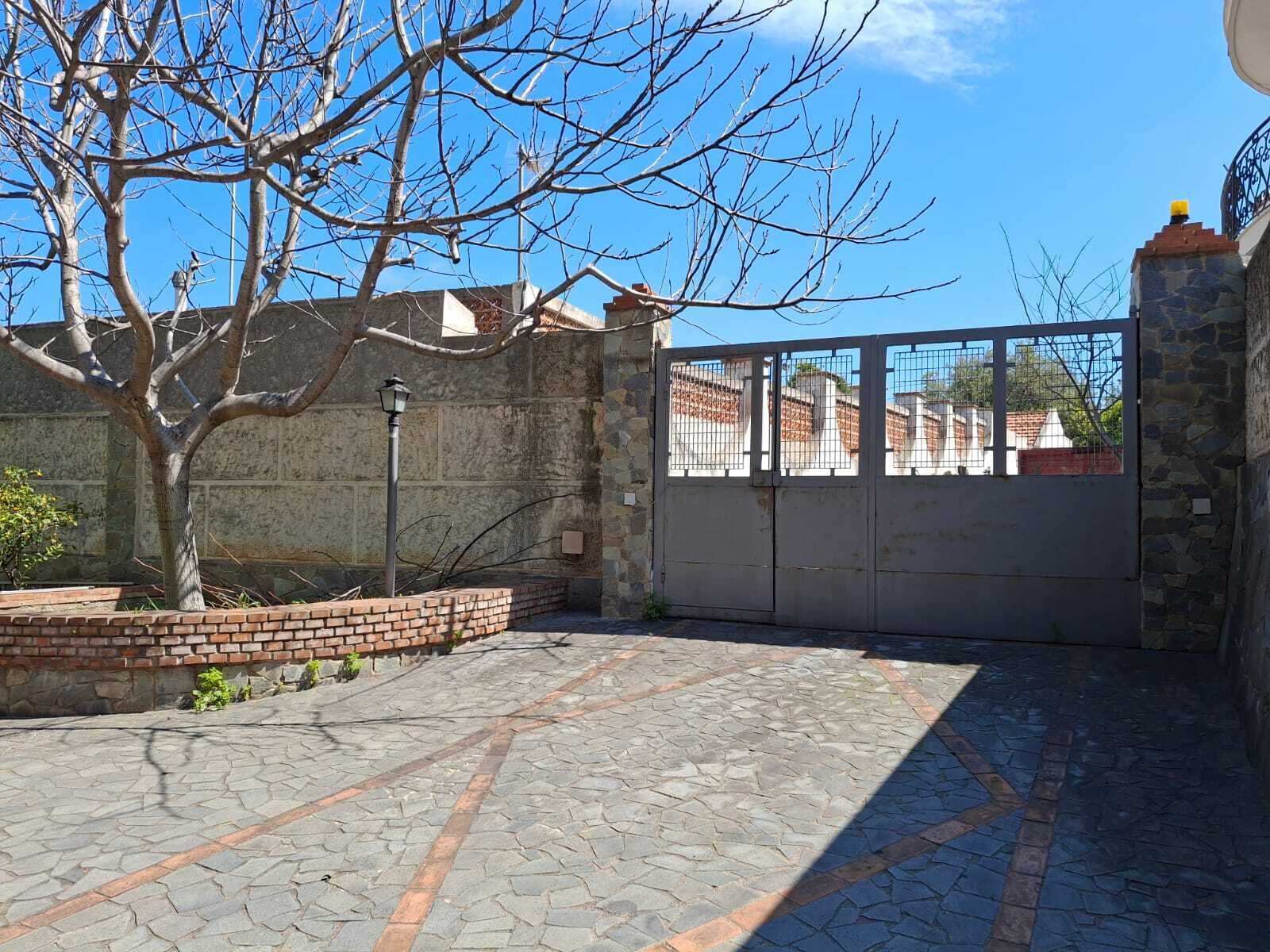 Ein gepflasterter Innenhof mit Steinmauer, Metallgitter und einem Baum.