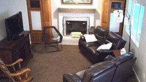 A living room with a fireplace, a leather sofa, a wooden chair, and a television on a cabinet. - Spacious 6-bedroom house with WiFi, fitness room in peaceful Thornton (Thornton)