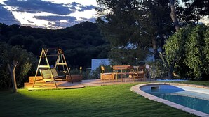 Un jardin avec une balançoire en bois, une piscine et un espace patio aménagé avec des chaises et des tables.
