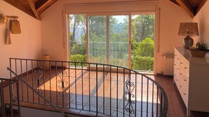 Un balcon spacieux offrant une vue sur la verdure, un plafond en bois et une commode blanche avec une lampe.