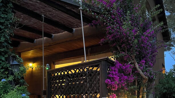 Un bâtiment doté d’un escalier en bois menant à une entrée abritée, entouré de plantes en fleurs et d’une clôture décorative.