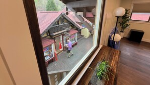 Una vista attraverso una finestra che mostra un edificio con una struttura dal tetto rosso, una scala e una pianta in vaso all'interno.