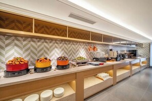 Montaje de bufé con diferentes alimentos y una cocina moderna al fondo.